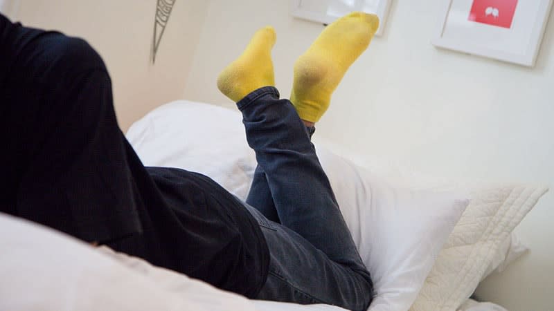 Yellow socks on person lying on bed with legs crossed