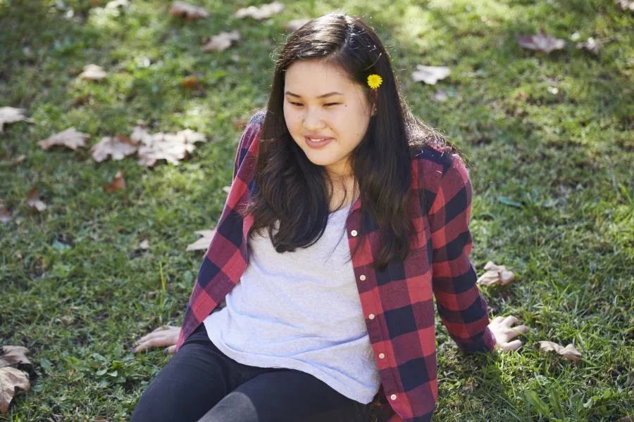 A girl with long dark brown hair sitting on the grass with a smile, looking relaxed.