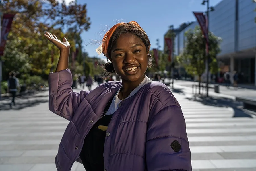 Henrietta girl smiling with raised hand and university walkway behind her