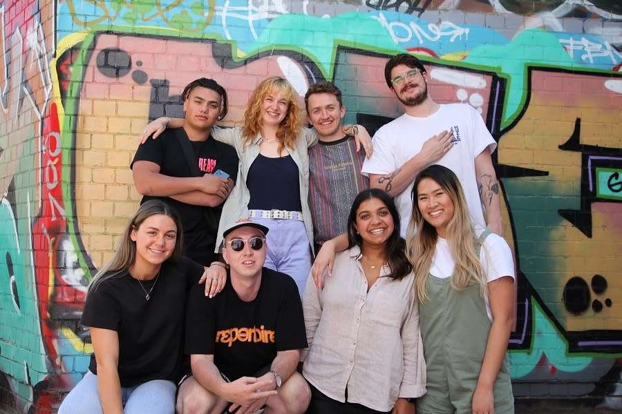 Group of young people sit in front of colourful building smiling