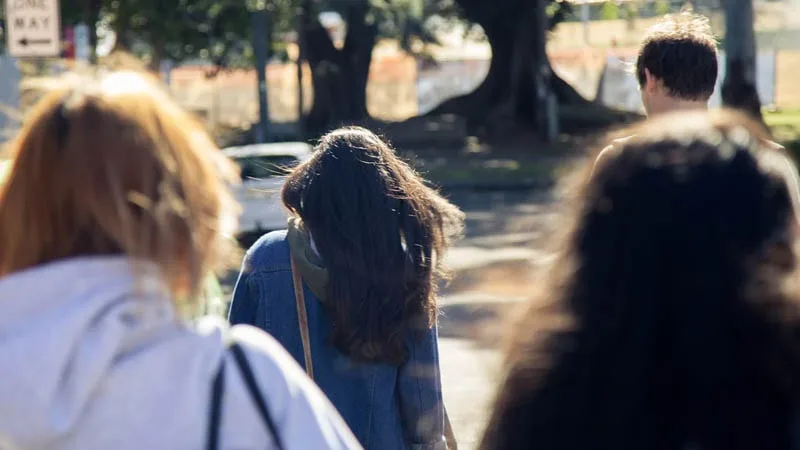 Photo from behind of group of friends walking down road towards a car. 