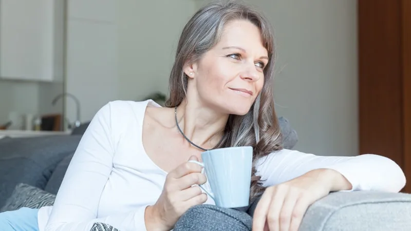 Mum looking happily into the distance on the couch holding a cup of tea