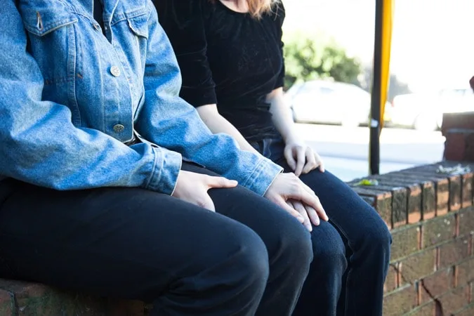 Headless girlfriends sitting on wall holding hands