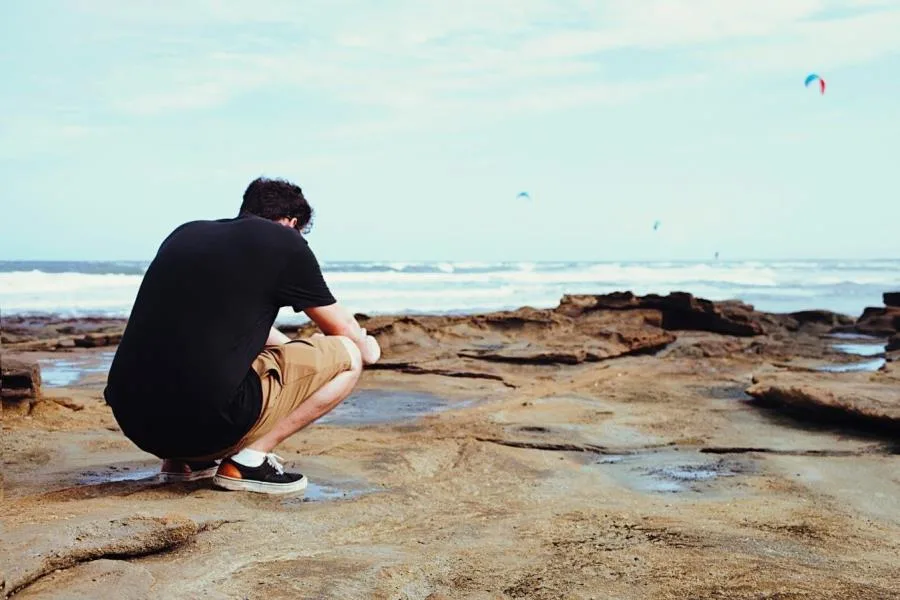 Boy with head down on ocean cliff