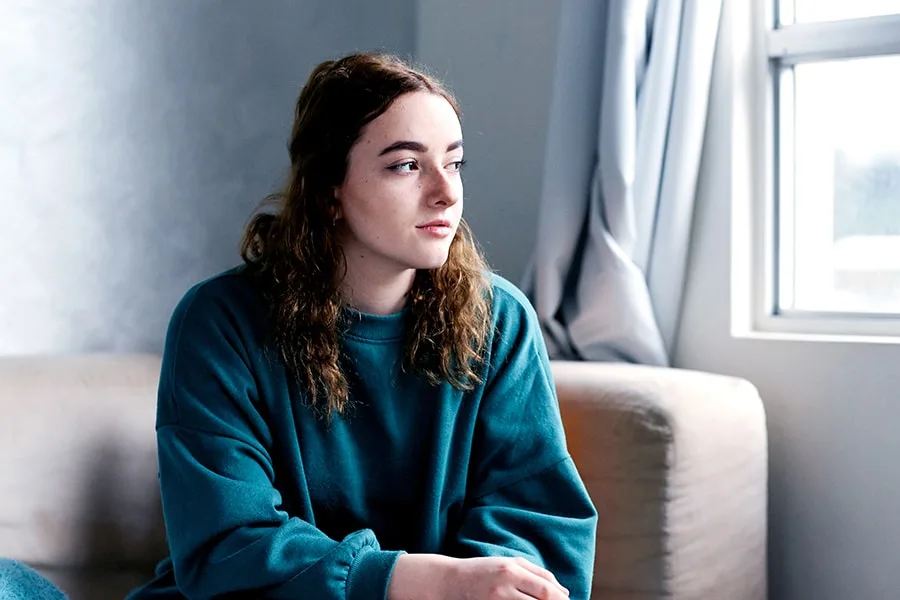 teenage girl sitting on couch looking out window