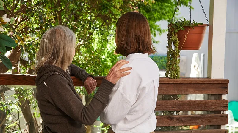 back view of mum with hand on teenage daughters shoulder standing together