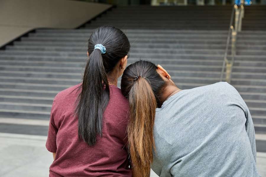 two girls sitting in front of a stairway and one of them leans on the other