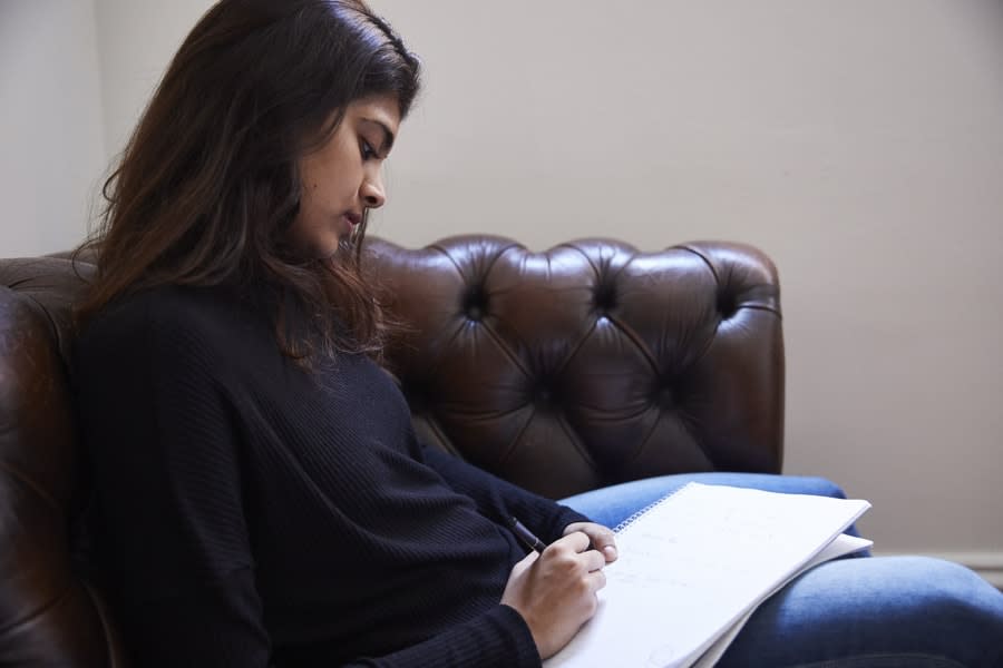 girl sitting on couch writing in notebook