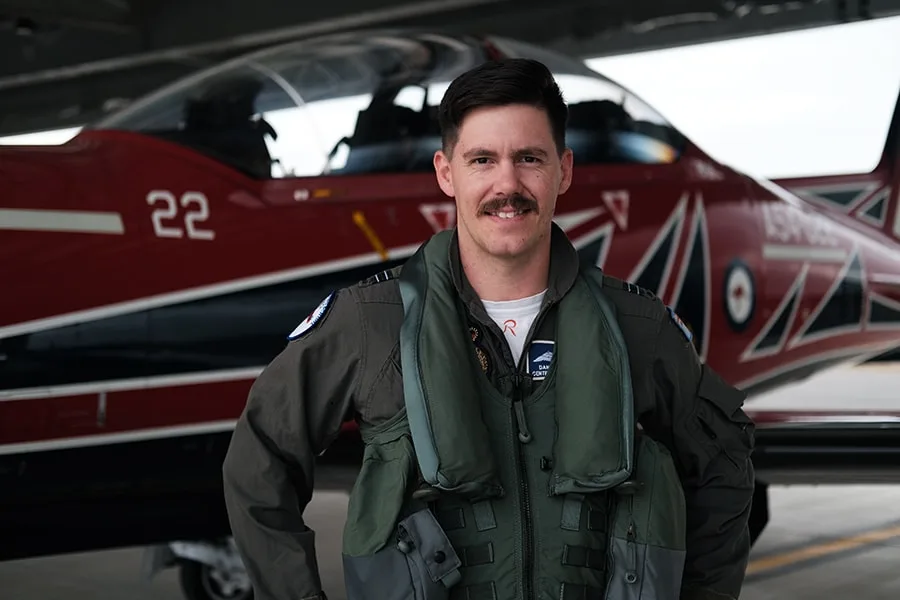 Dan guy wearing pilots jacket with airplane behind him