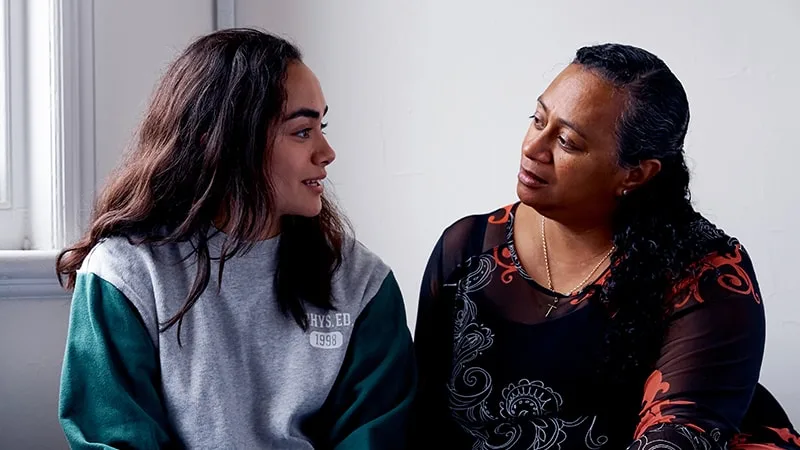 girl and mother in casual clothes sitting on bed talking