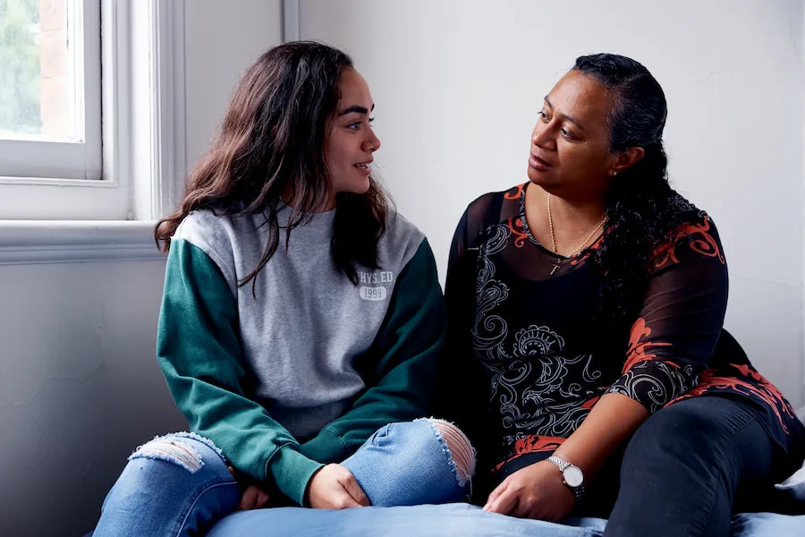 Image of a mother and daughter sitting on bed talking.