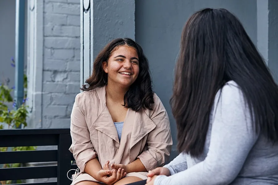 girl smiling talking to her friend on a bench outside