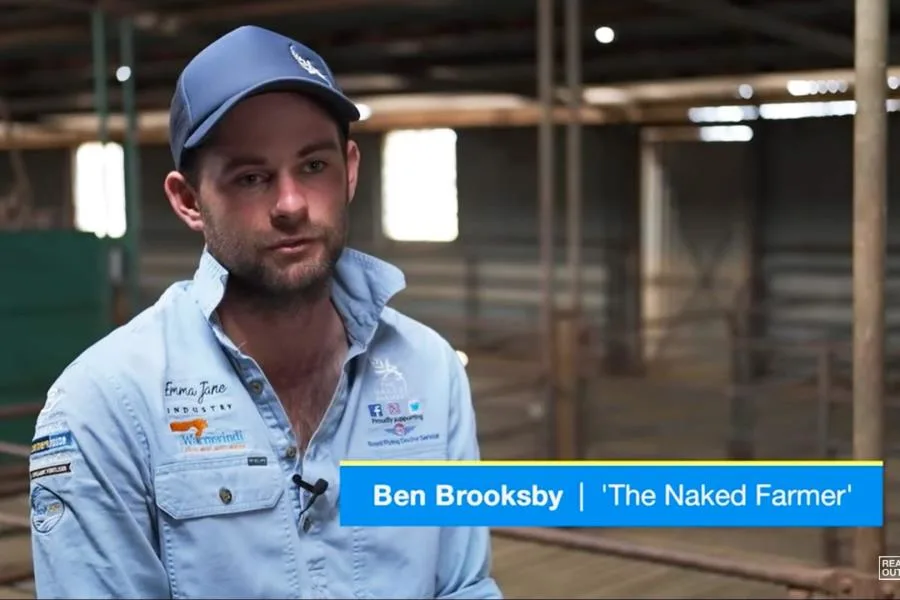 the naked farmer man wearing casual shirt and cap talking to camera in a stable