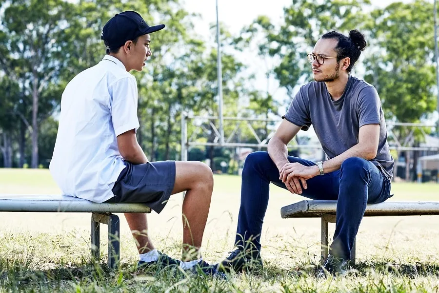 Boy in hat talking to youth worker on bench