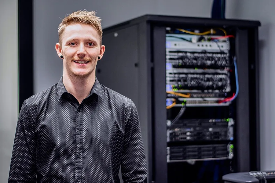 Brodie guy in button up collared shirt with office server behind him