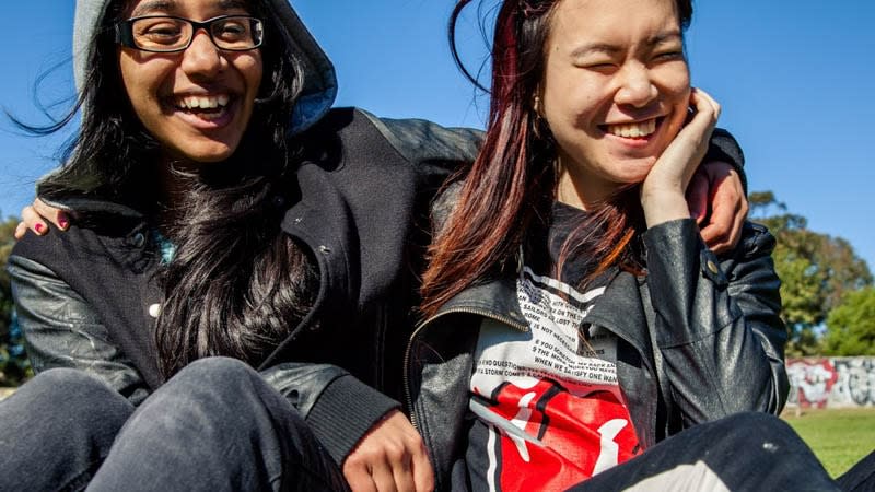 Two girls laughing in park with arms around each other