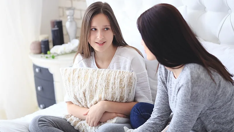 Mother and daughter talking sitting on bed