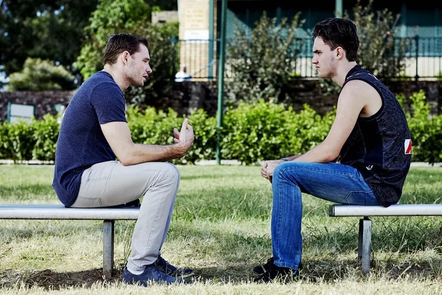 Counsellor in blue shirt talking to boy on metal bench