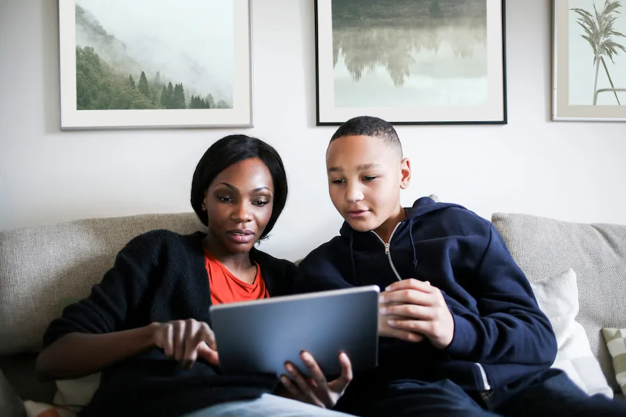 Image of a mum and child leaning in close to each other on a couch looking at a tablet together.