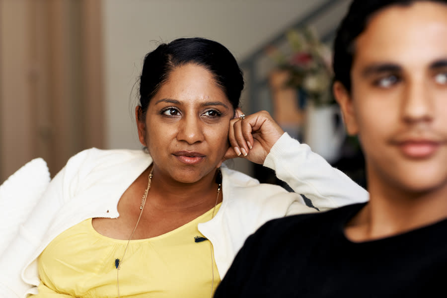 Image of a woman with neutral expression sitting on couch, looking over her son's shoulder.
