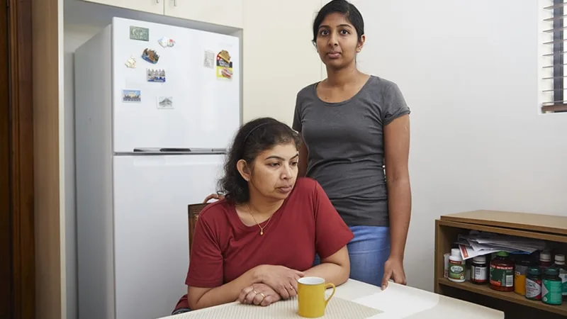 a mother sitting at a kitchen table with teenager standing next to her