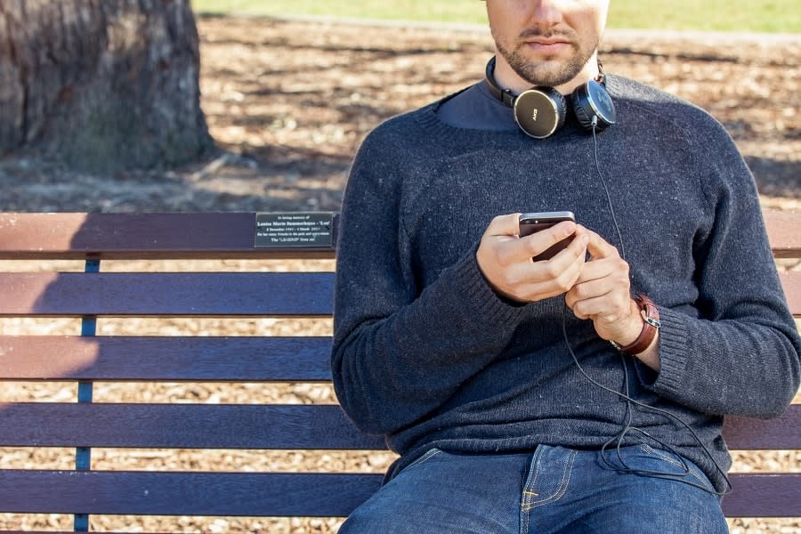 Close up of guy sitting on park bench using his phone