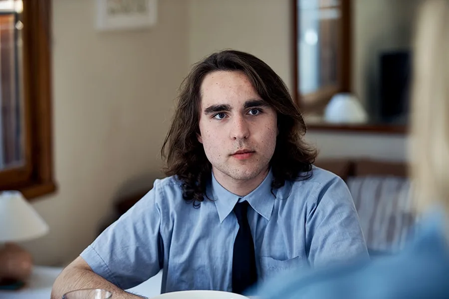 young guy in school shirt and tie talking to offscreen girl