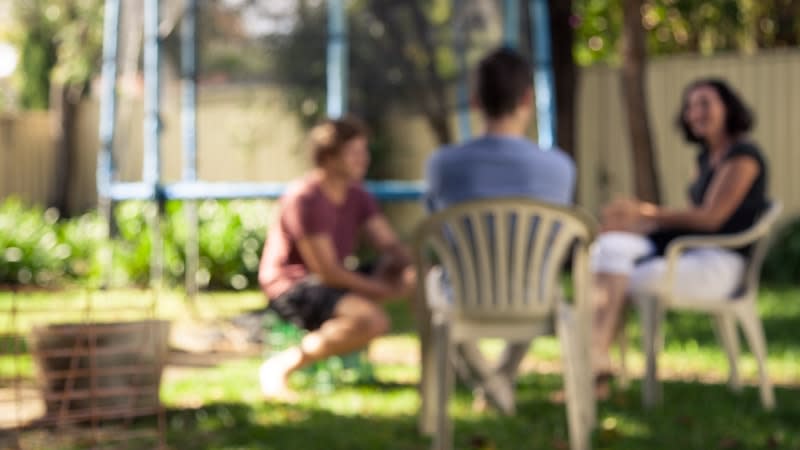 a blurred photo of three people having a discussion in a backyard