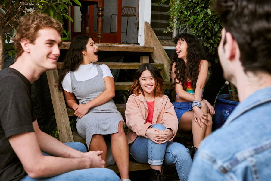 Five friends sitting together outside, smiling and laughing.