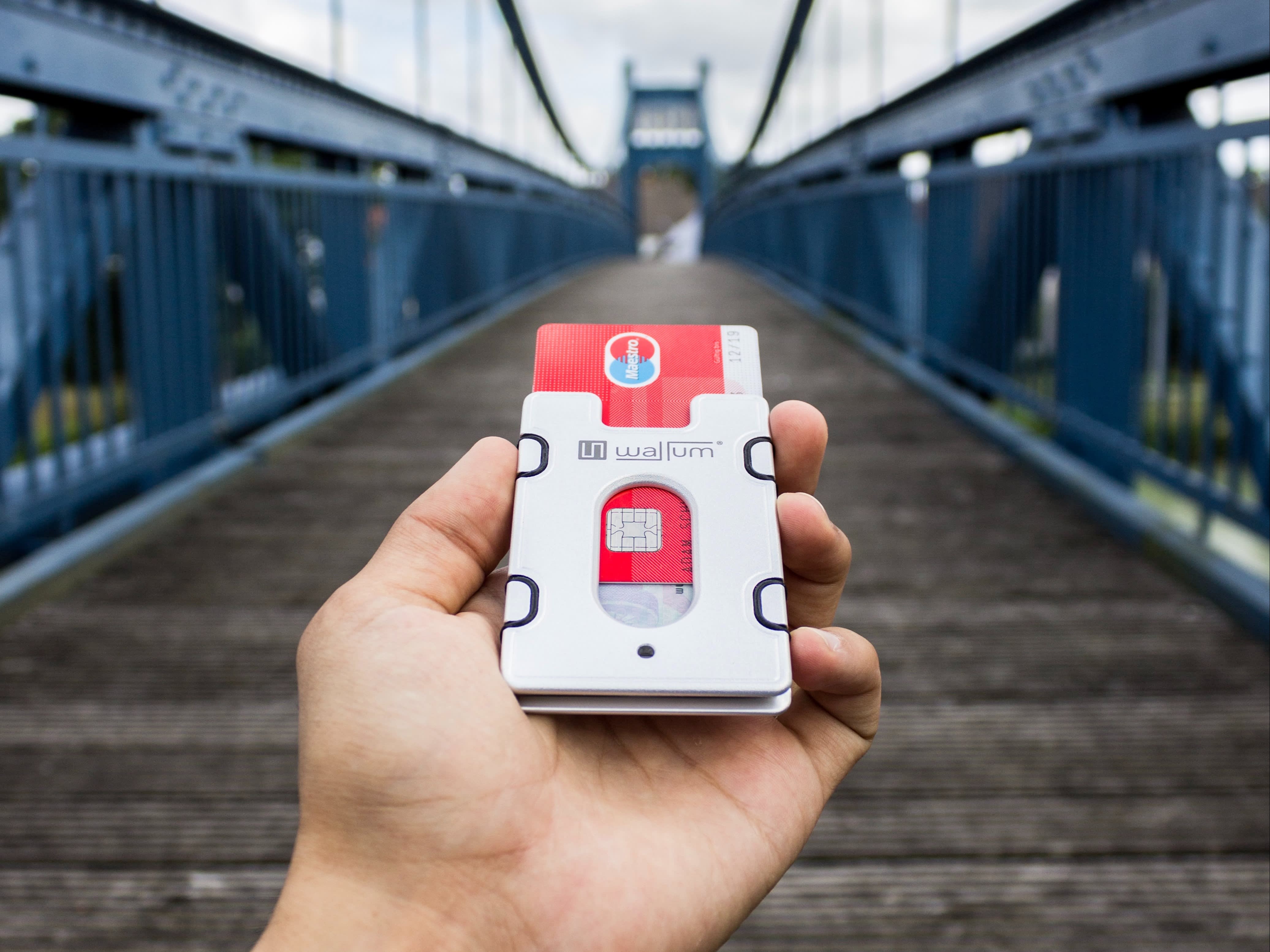 A hand holding a debit card. The picture has a view of a bridge.