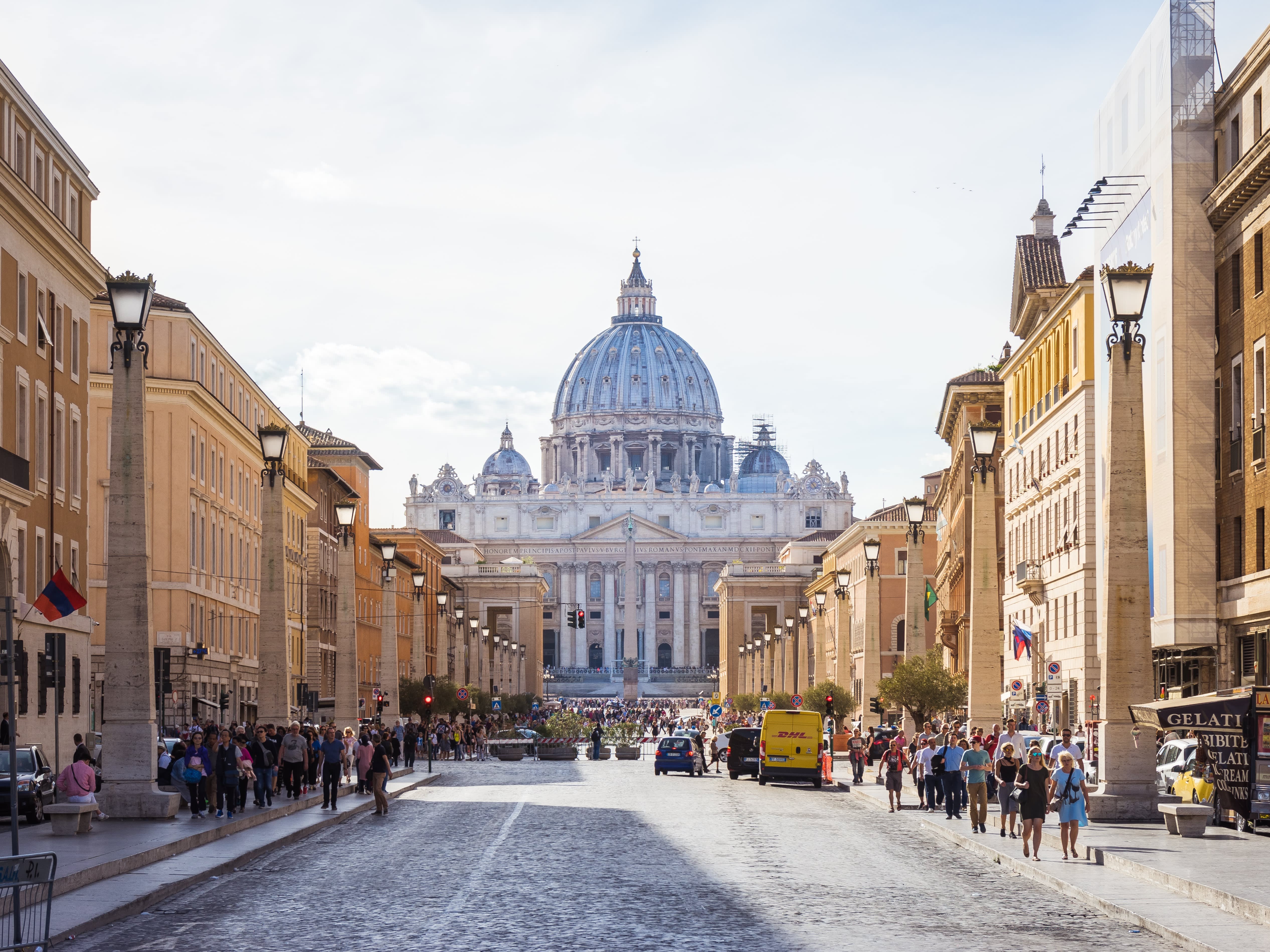 A picture of the boulevard filled with people leading up to the Saint Peter's Basilica taken on a sunny day.