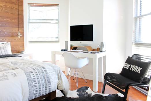 Bright student room with iMac on the desk and white chair and big size comfy bed in front a black chair with New York black pillow