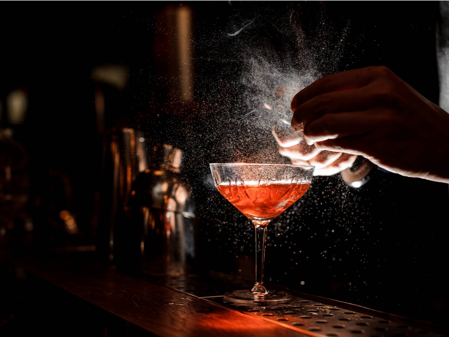 Bartender sprinkling juice into a cocktail glass