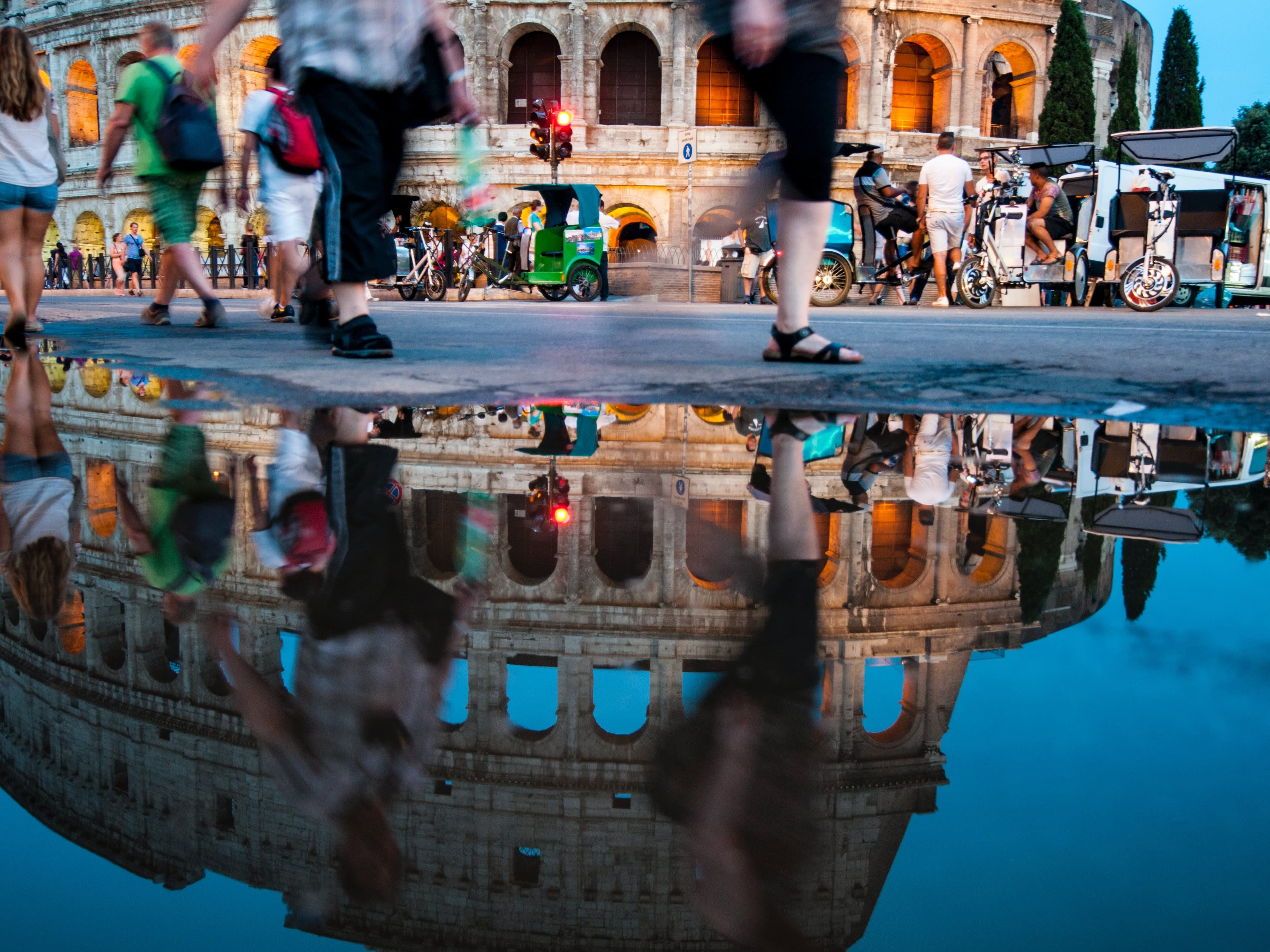 A picture of the reflection of the colosseum Rome with people walking across the frame
