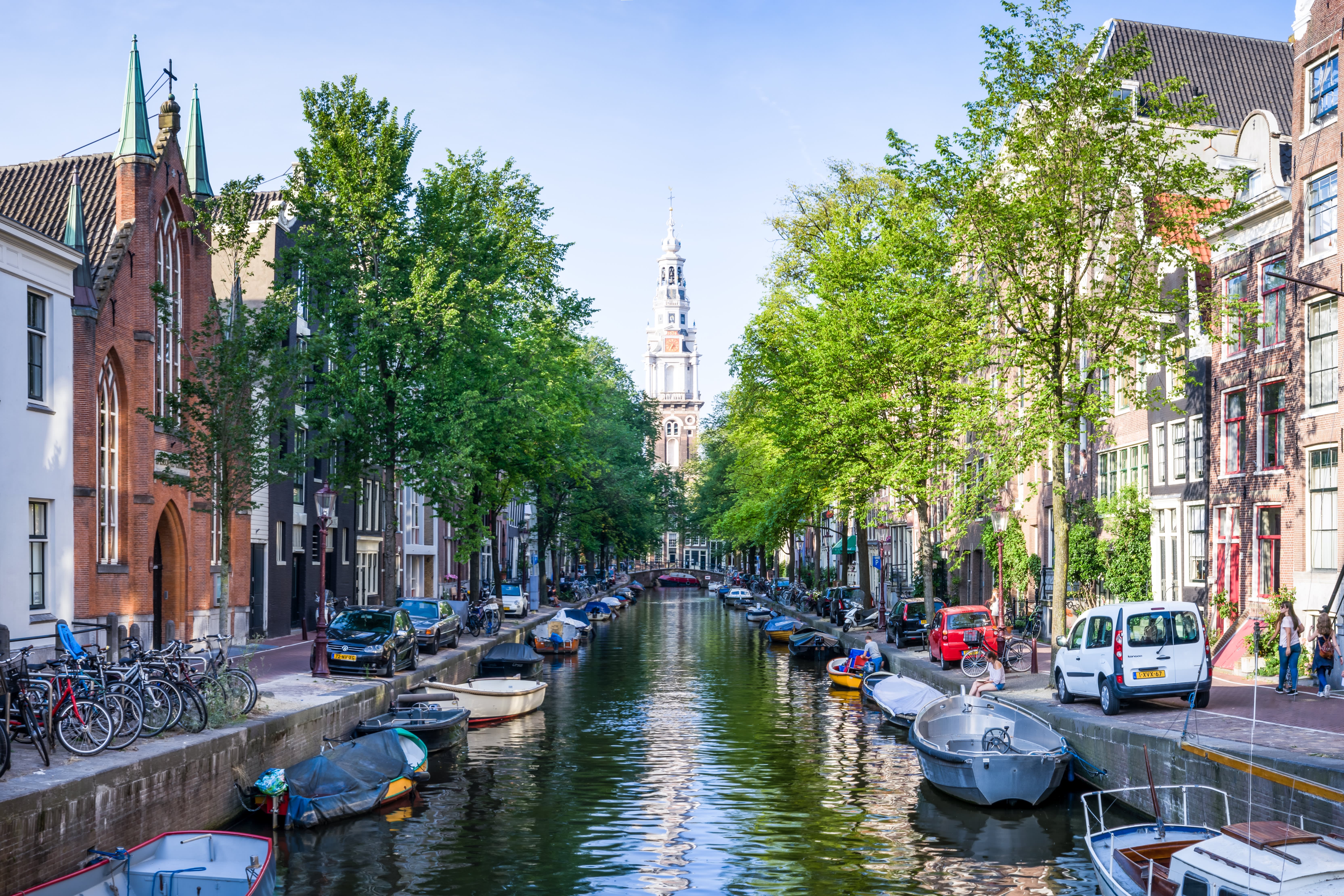 Image of a canal in Amsterdam Centrum, with boats and a church bell tower on the background