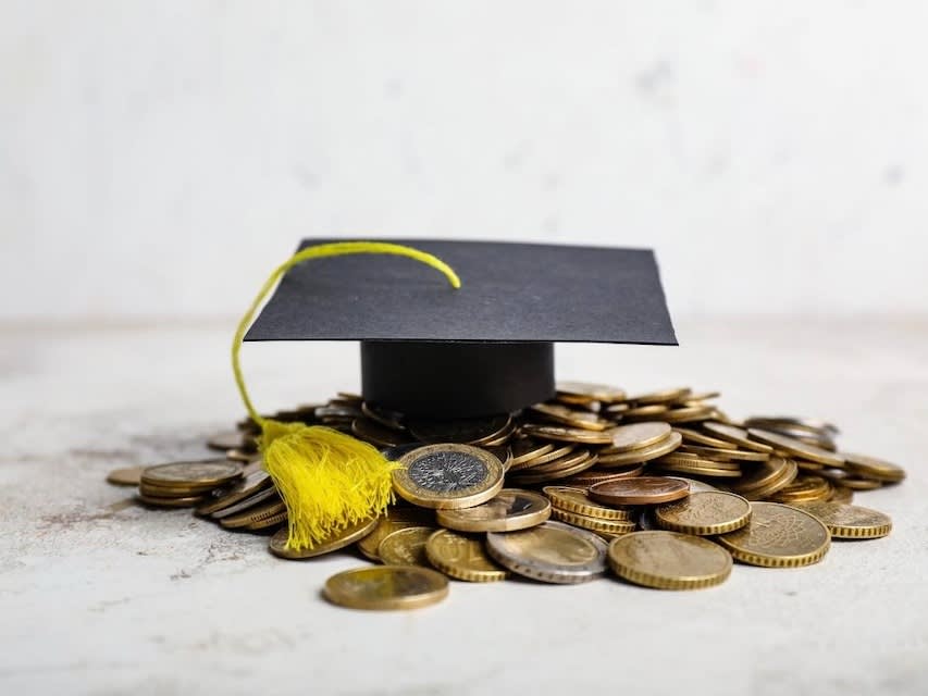 A tiny replica of a graduation cap with a pile of coins around it symbolizing the tuition fees for universities in Italy
