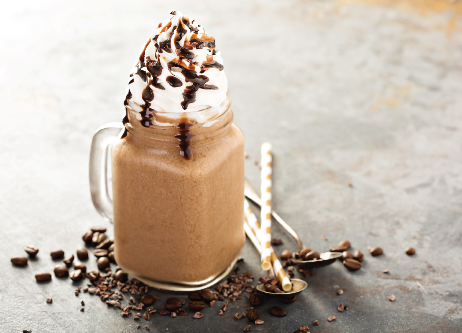 A photo of a Coffee in a glass with cream, and chocolate sauce on top surrounded by coffee beans