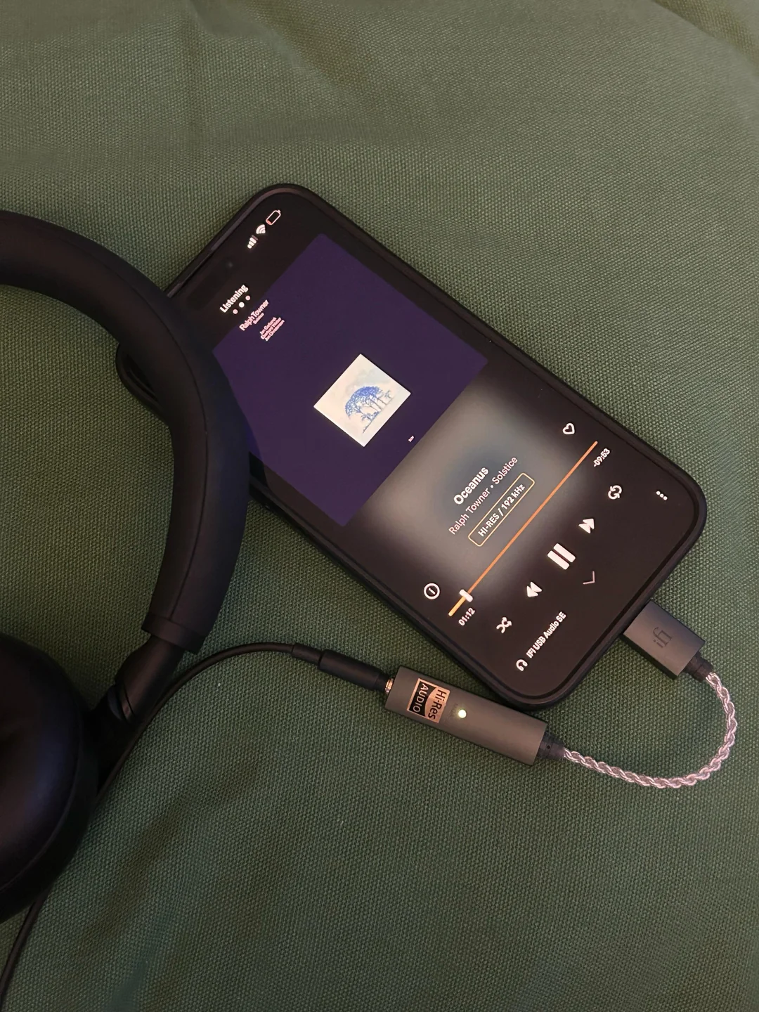 A phone connected to wired headphones through a small DAC displays a high-resolution Qobuz recording.