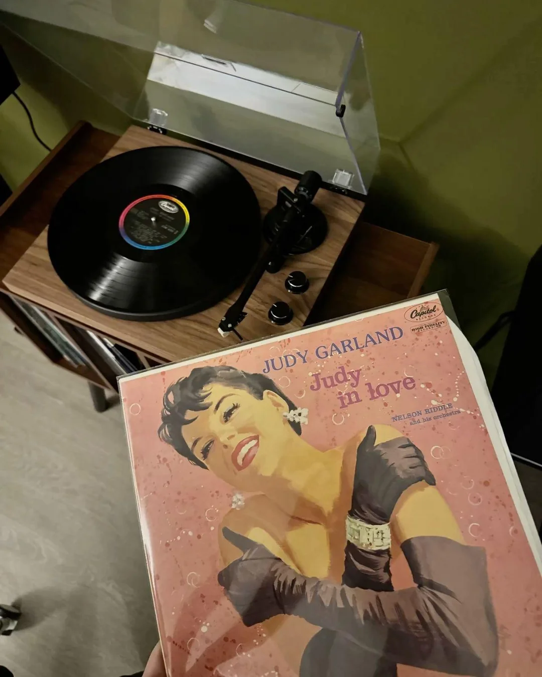 A Judy Garland record sleeve is held in front of a wooden turntable playing a vinyl record.