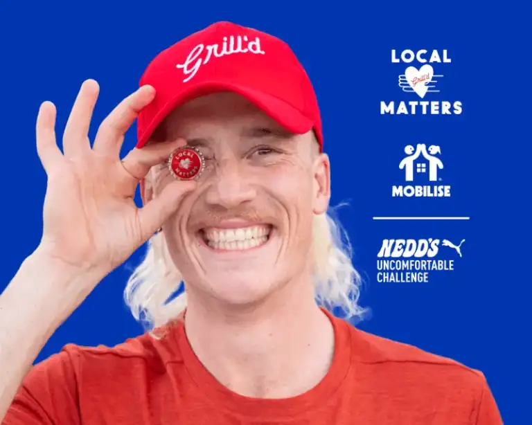 Nedd Brockman smiling & holding a Local Matters Token in front of his eye