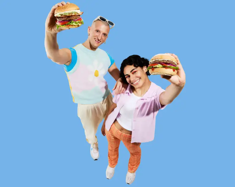 Two young people holding burgers on a blue background