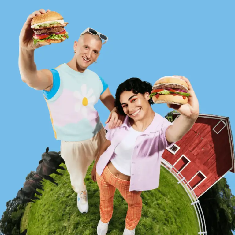 Two young people standing on a sphere holding burgers