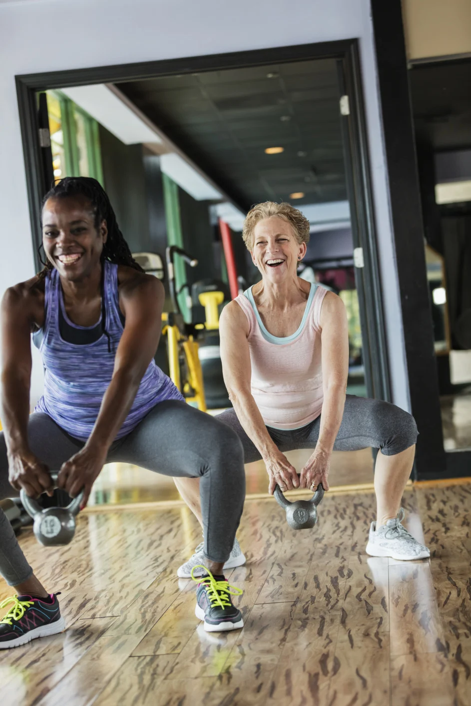 Fitness Trainer with a mature client squatting with kettlebells