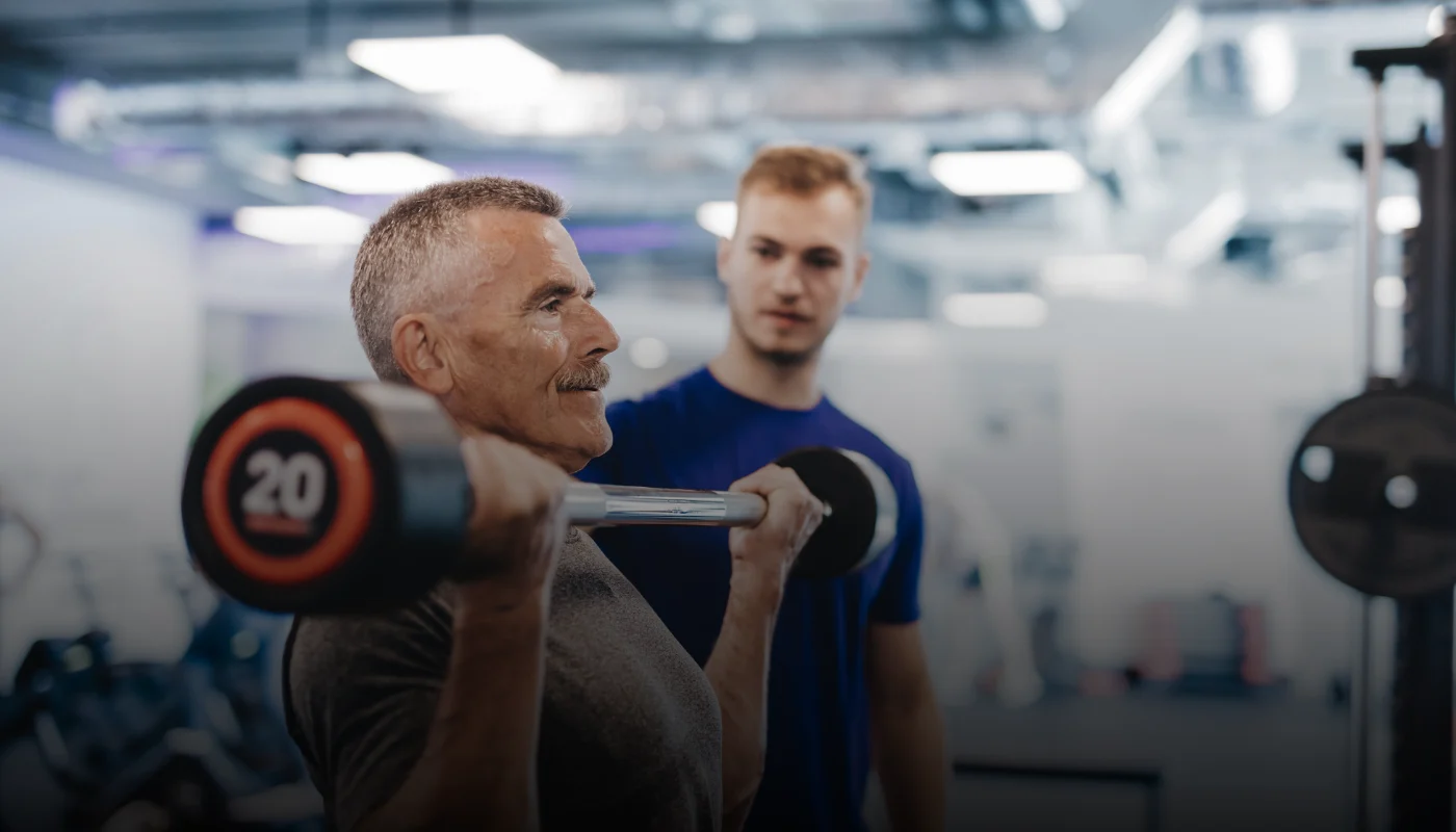 ISSA trainer helping senior client lift weights.