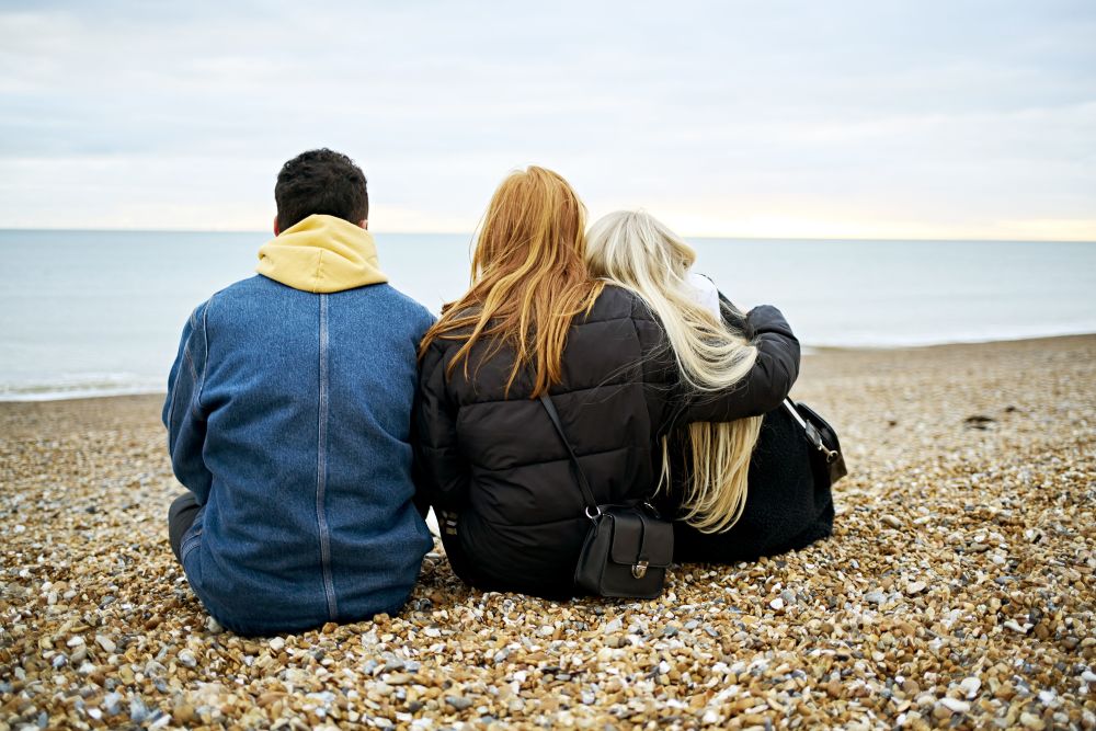 Three friends sat on beach looking out to sea 