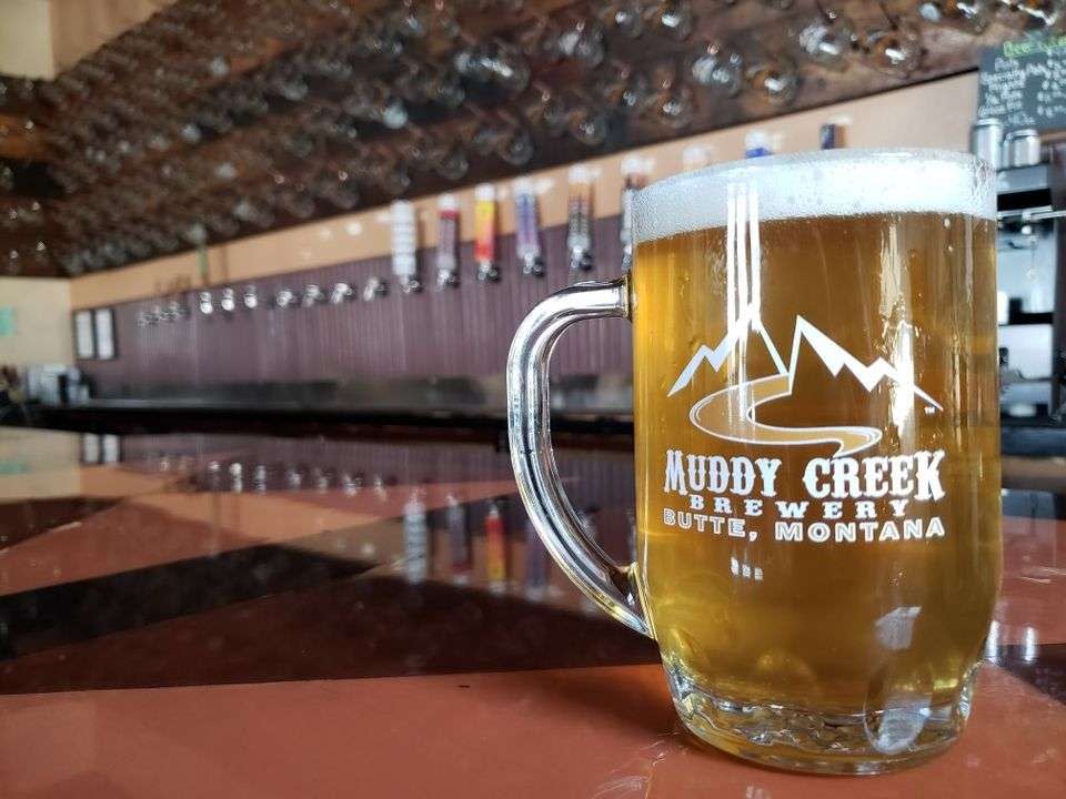 A picture of a mug of beer in front of beer taps at Muddy Creek Brewery