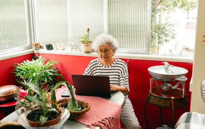 An elderly woman studying law on her laptop inside a bright sunroom