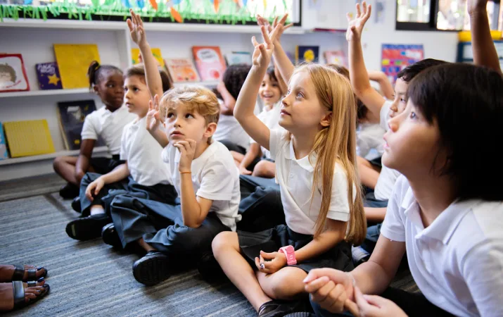 Primary school children raising their hands and engaged with their teacher in the classroom
