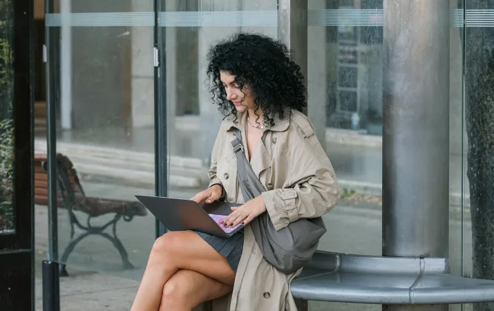 A woman using a laptop while seated outside a modern building.