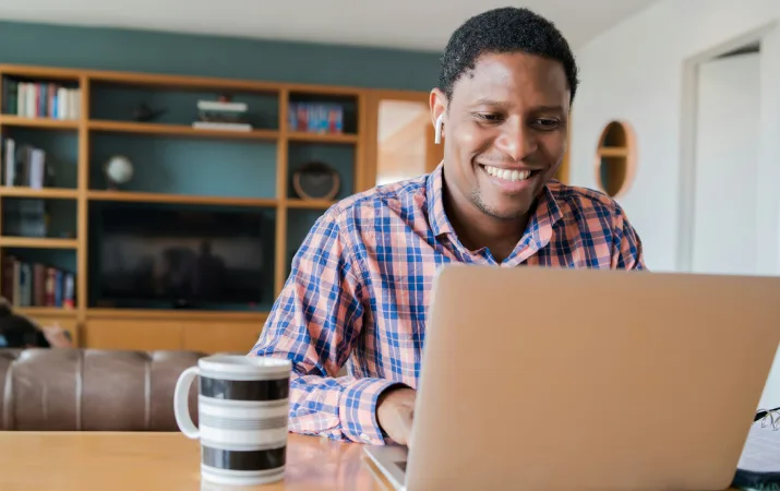 Smiling man with airpods and a mug of coffee studying on laptop